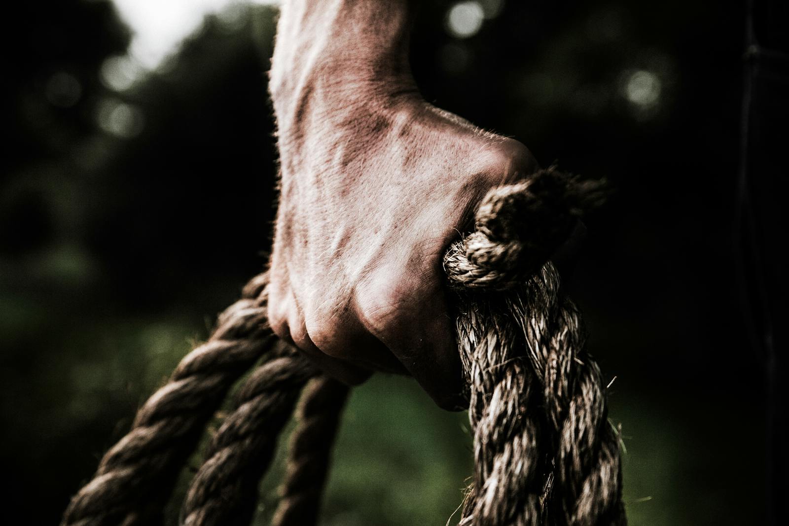A close-up image shows a strong, firm hand gripping a thick, rough rope, showcasing strength and determination in an outdoor setting.