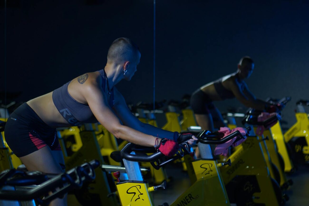 A woman exercising on a stationary bike in a dimly lit gym, focused on fitness and endurance.