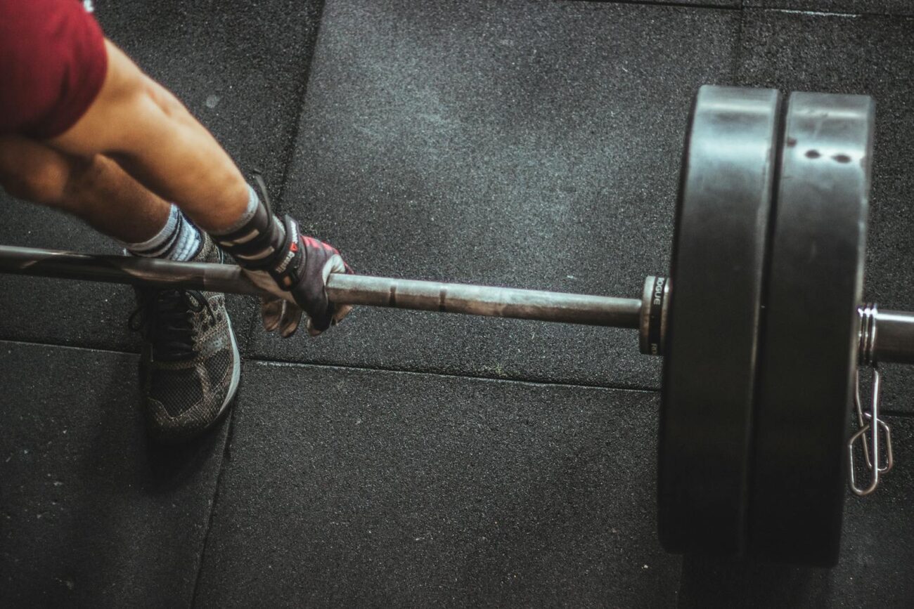 Close-up of muscular arm lifting barbell in gym, showcasing strength and fitness.