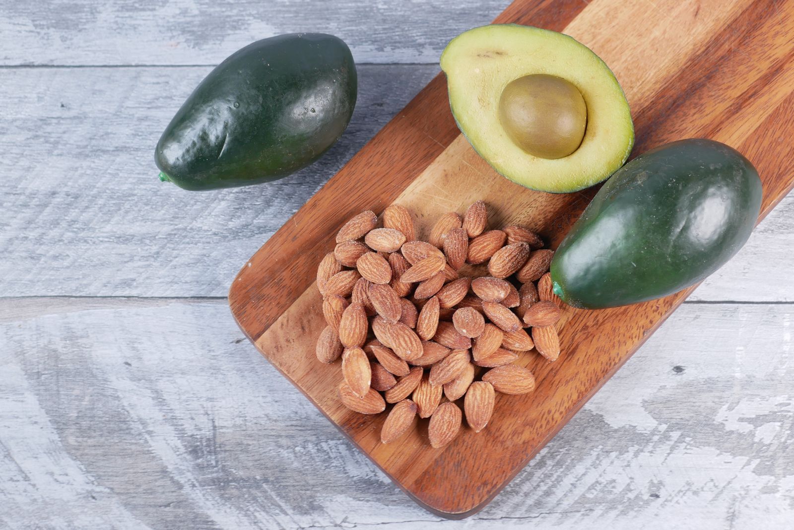 Avocados and almonds on a wooden board, showing healthy fats that add satisfaction to meals and support recovery