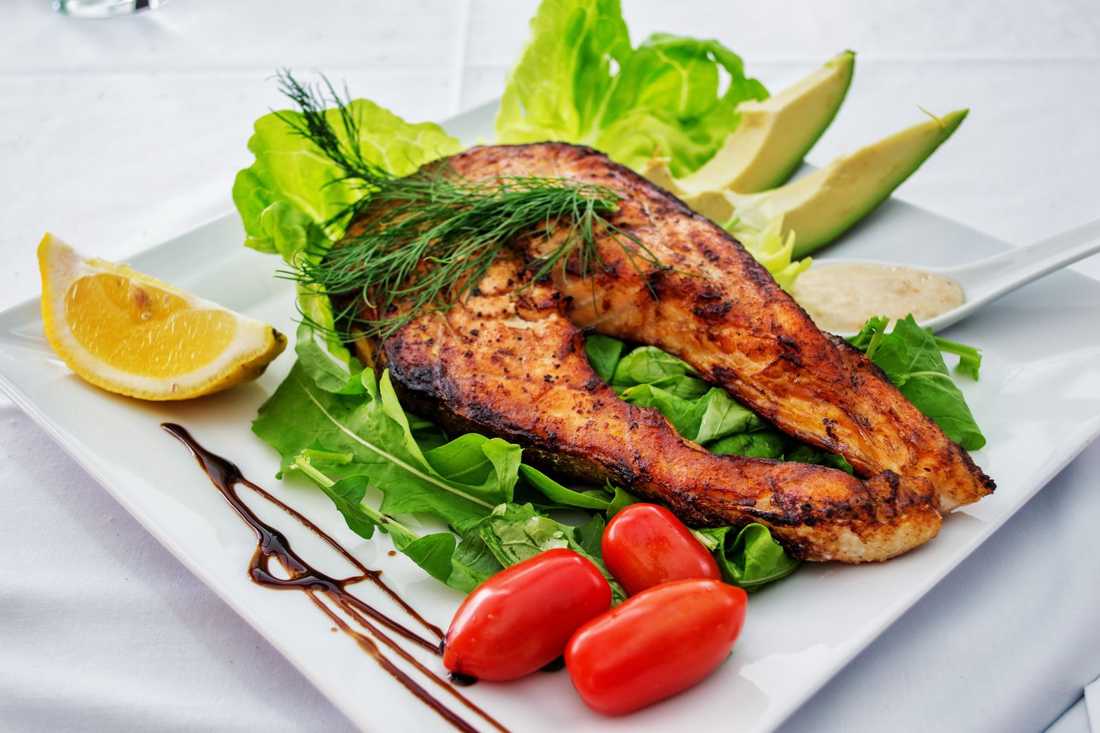 A plated salmon fillet with fresh greens, tomatoes, and avocado, showing a balanced whole-food meal for losing weight