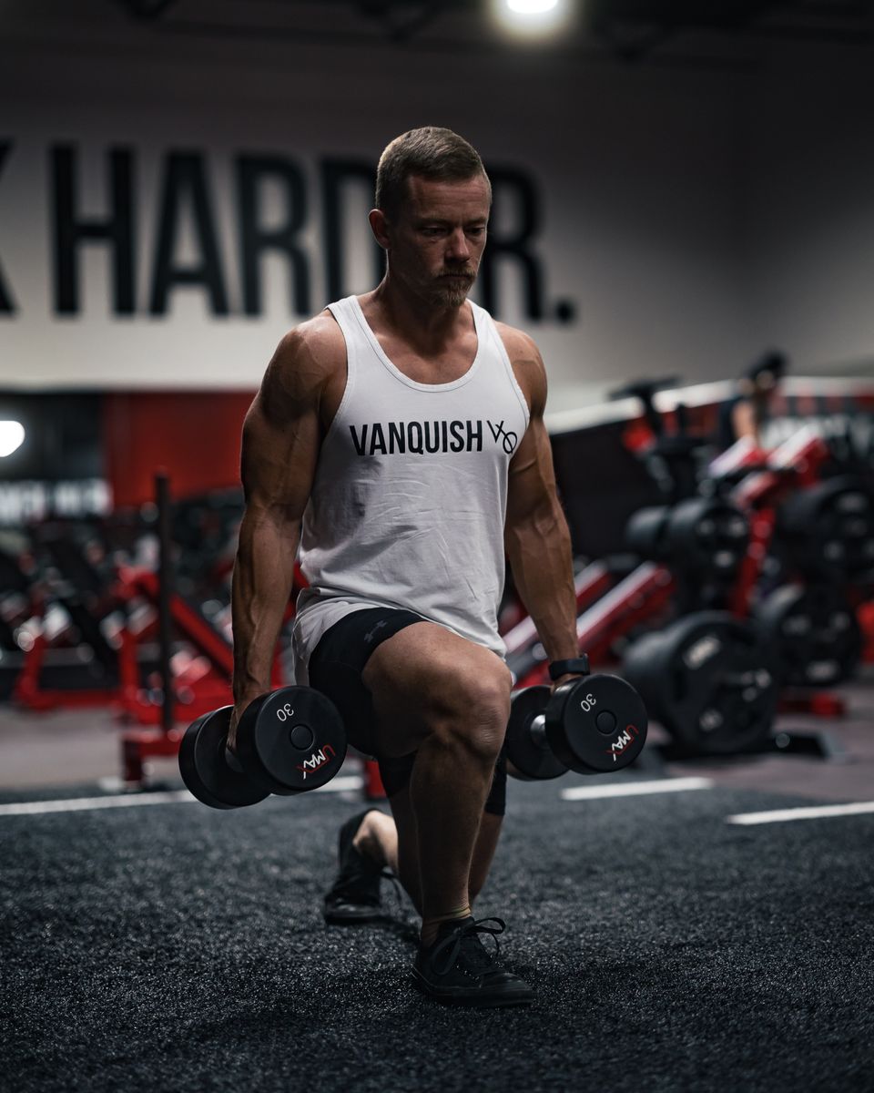 A lifter performing weighted dumbbell lunges in a gym, the kind of real load legs need to grow