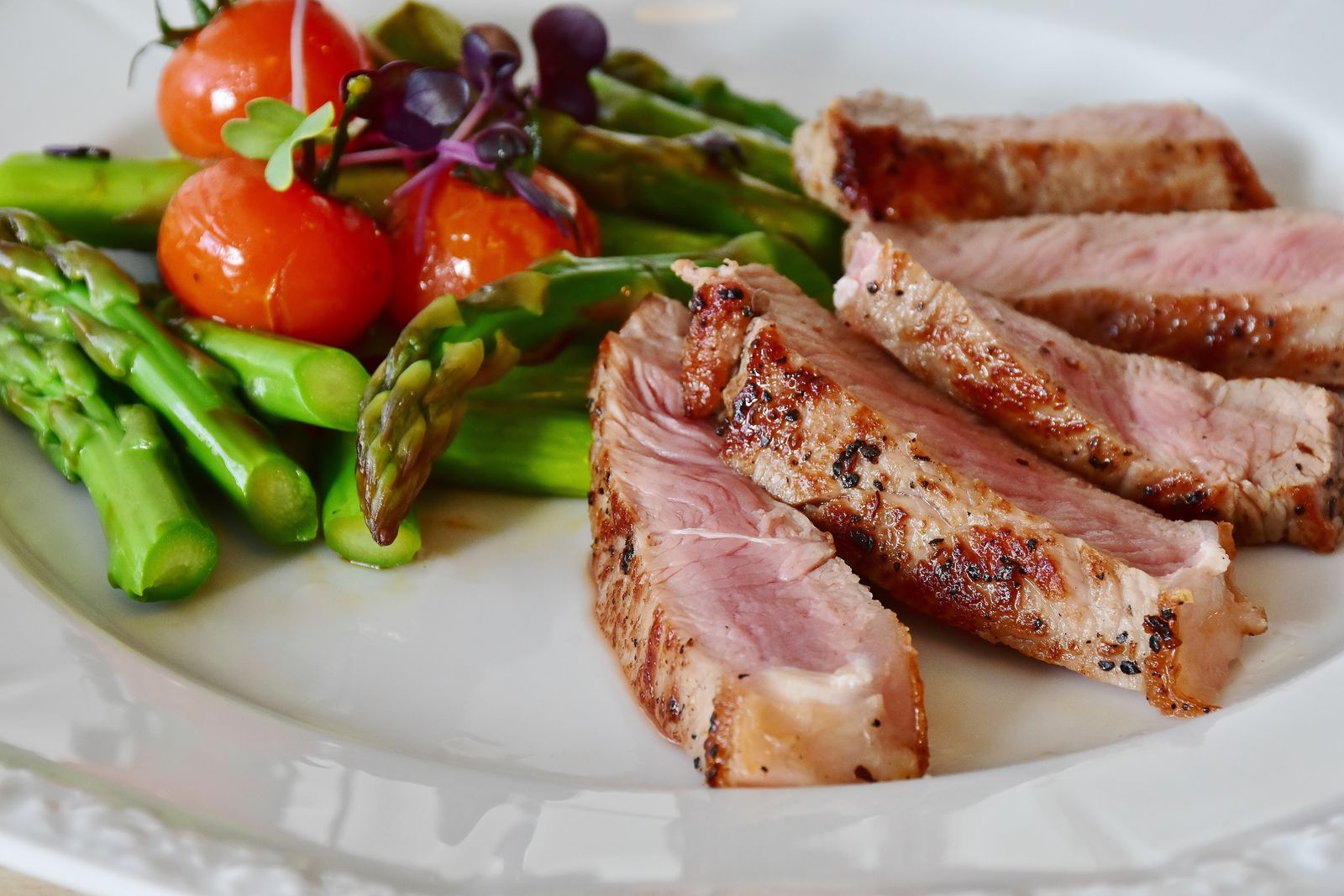A plate of sliced steak with asparagus and tomatoes, showing the kind of whole-food eating that drives fat loss