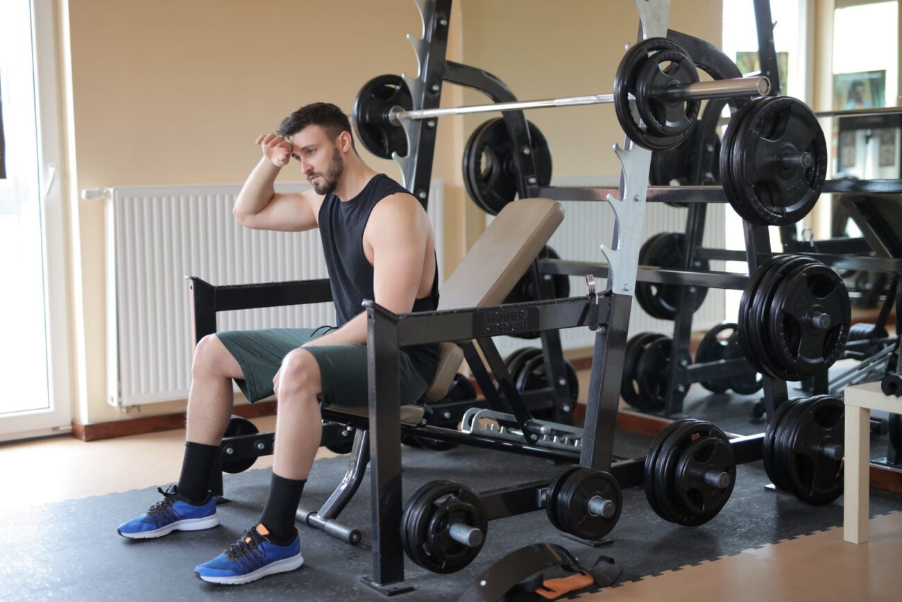 A man sitting on a gym bench looking tired during a workout, illustrating the fatigue that can come with fasted training