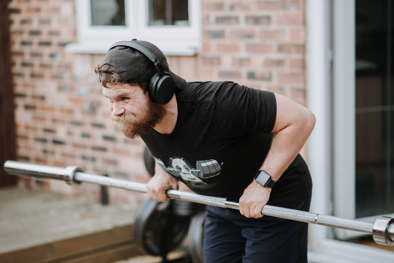A man performing a barbell row at home, illustrating progressive overload and consistent training effort
