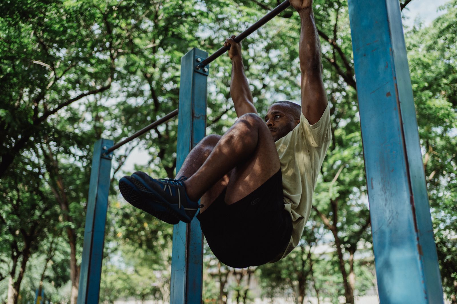  Man doing hanging leg raises on an outdoor bar to train the core