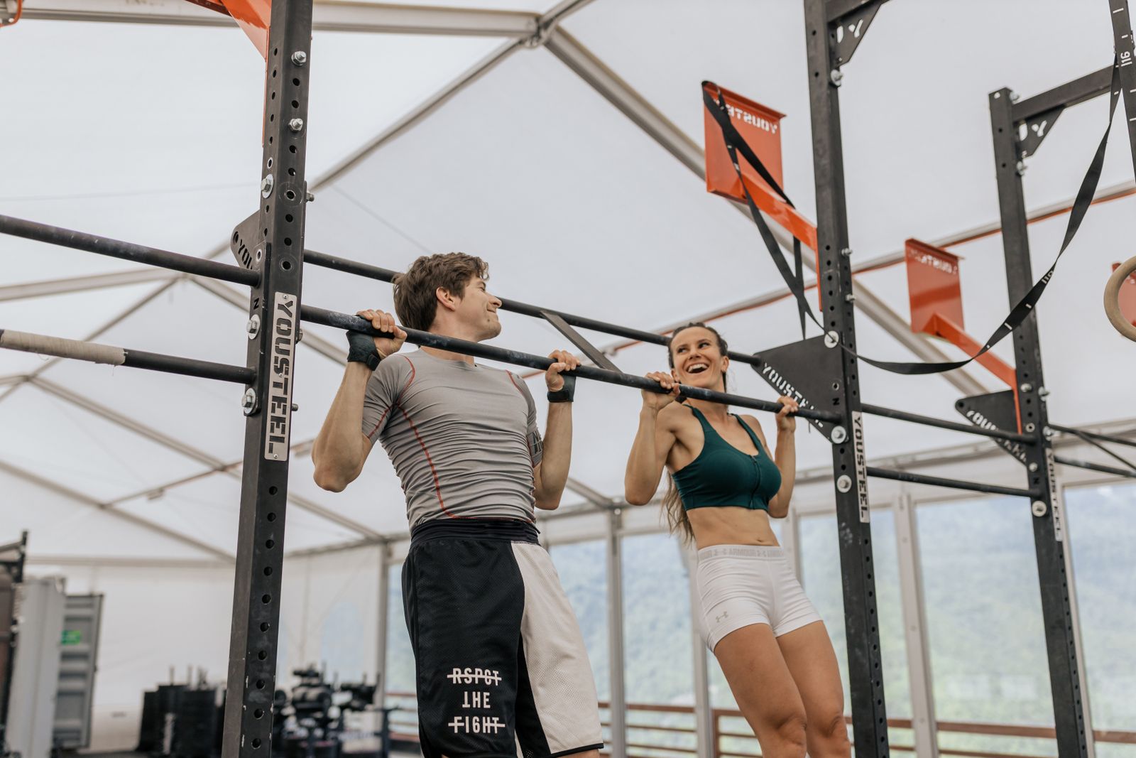 Two people training pull-ups together on a gym bar