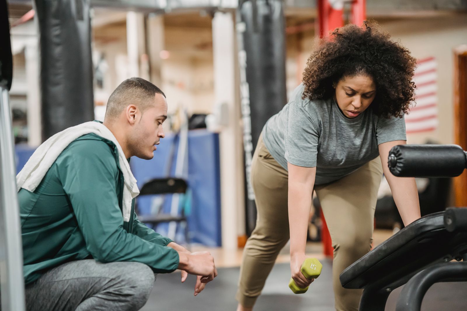 A beginner learning a dumbbell exercise with guidance, showing the focus on proper form when starting out
