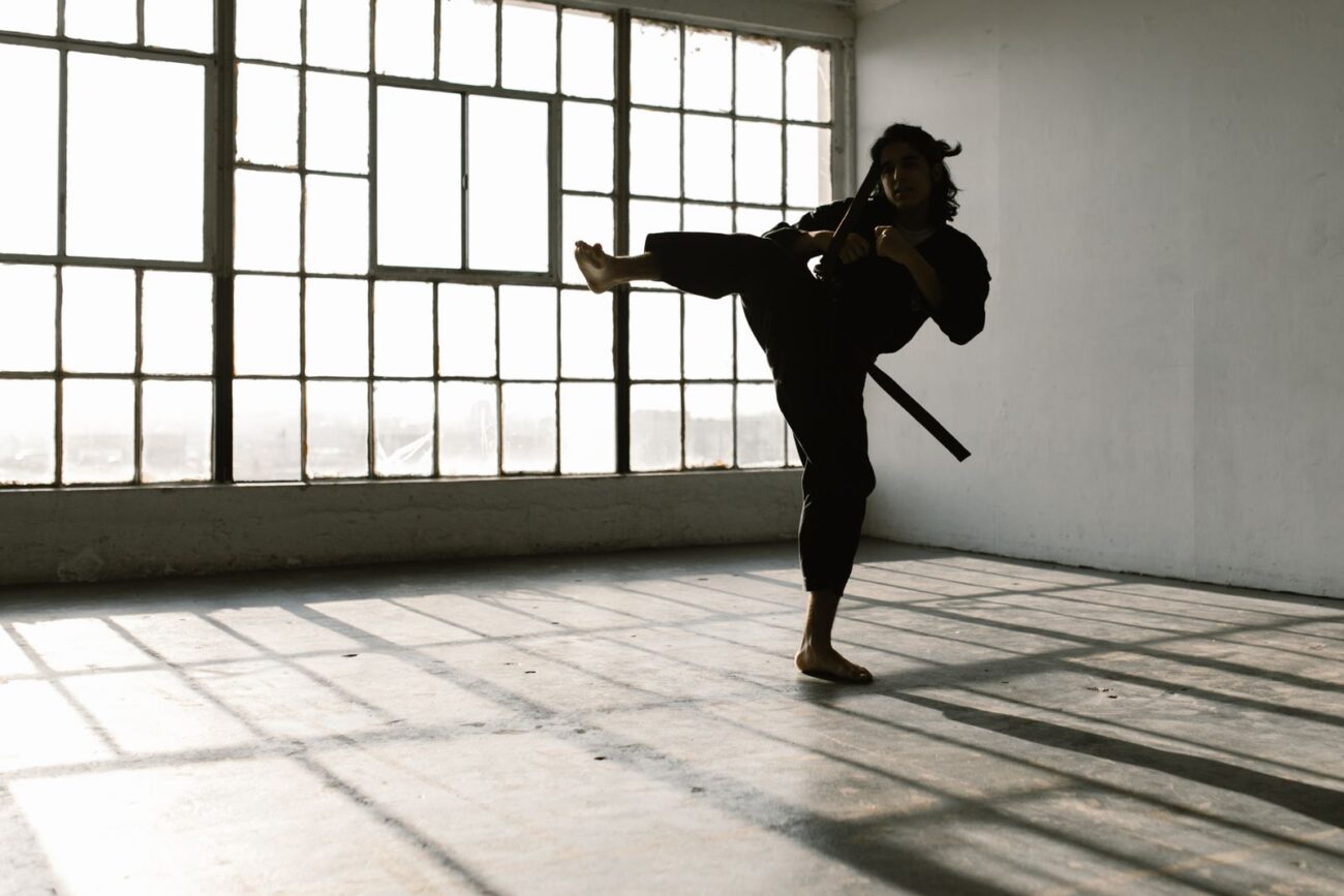 A person performing a high kick in an empty room, showing the athletic movement and discipline a challenging sport builds