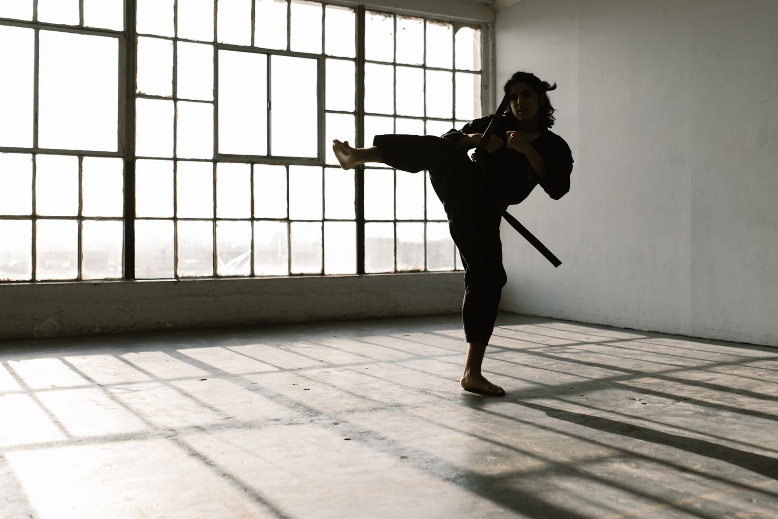 A person performing a high kick in an empty room, showing the athletic movement and discipline a challenging sport builds