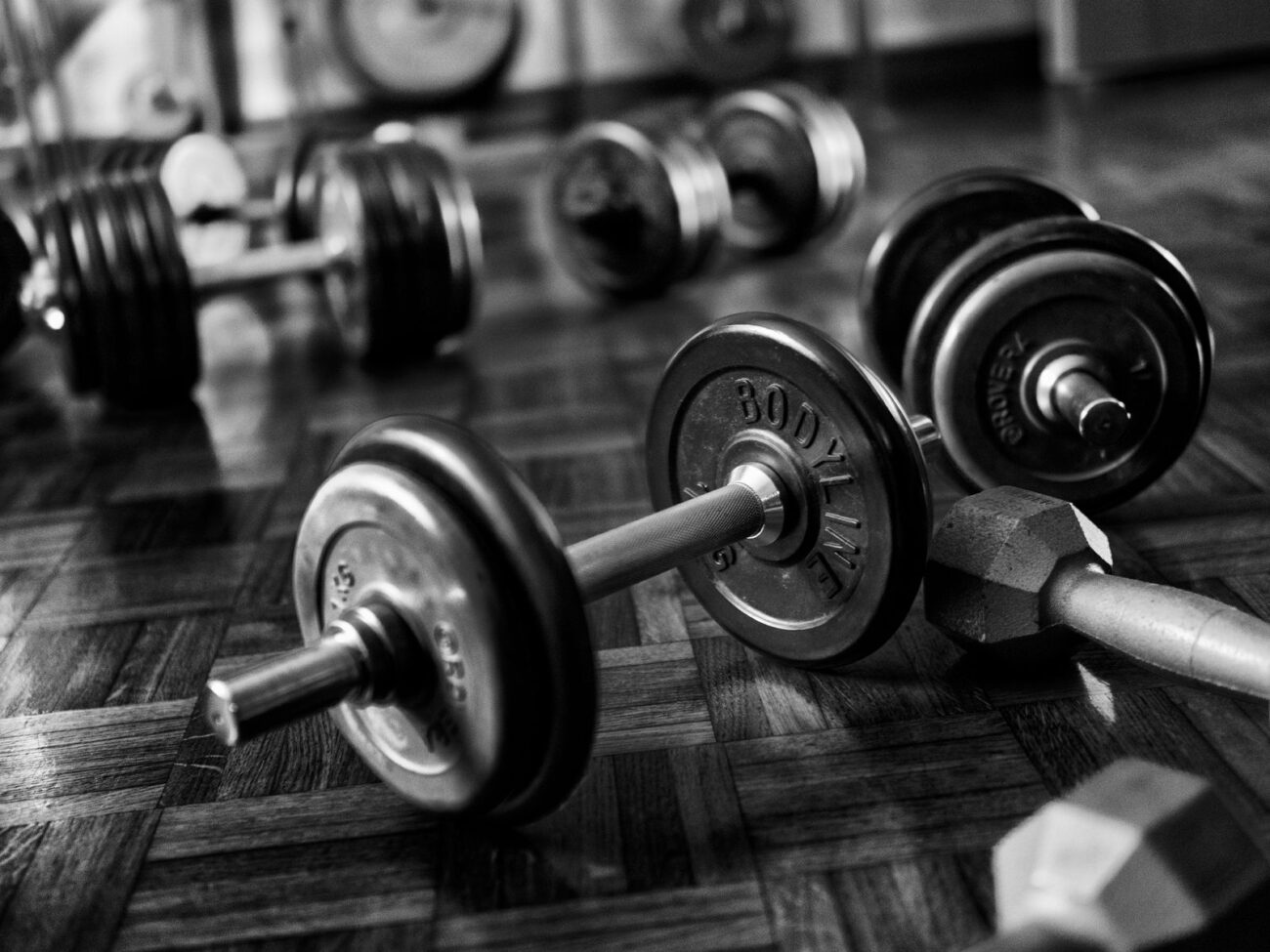 Basic dumbbells and loaded barbells on a wooden floor, showing that real results come from the work, not a fancy gym