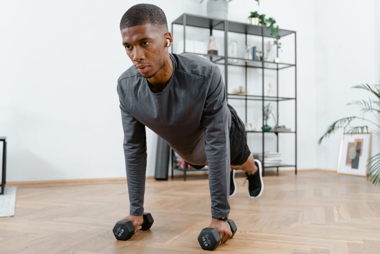 A man training at home with dumbbells in a focused plank position, showing the everyday consistency behind natural lifting