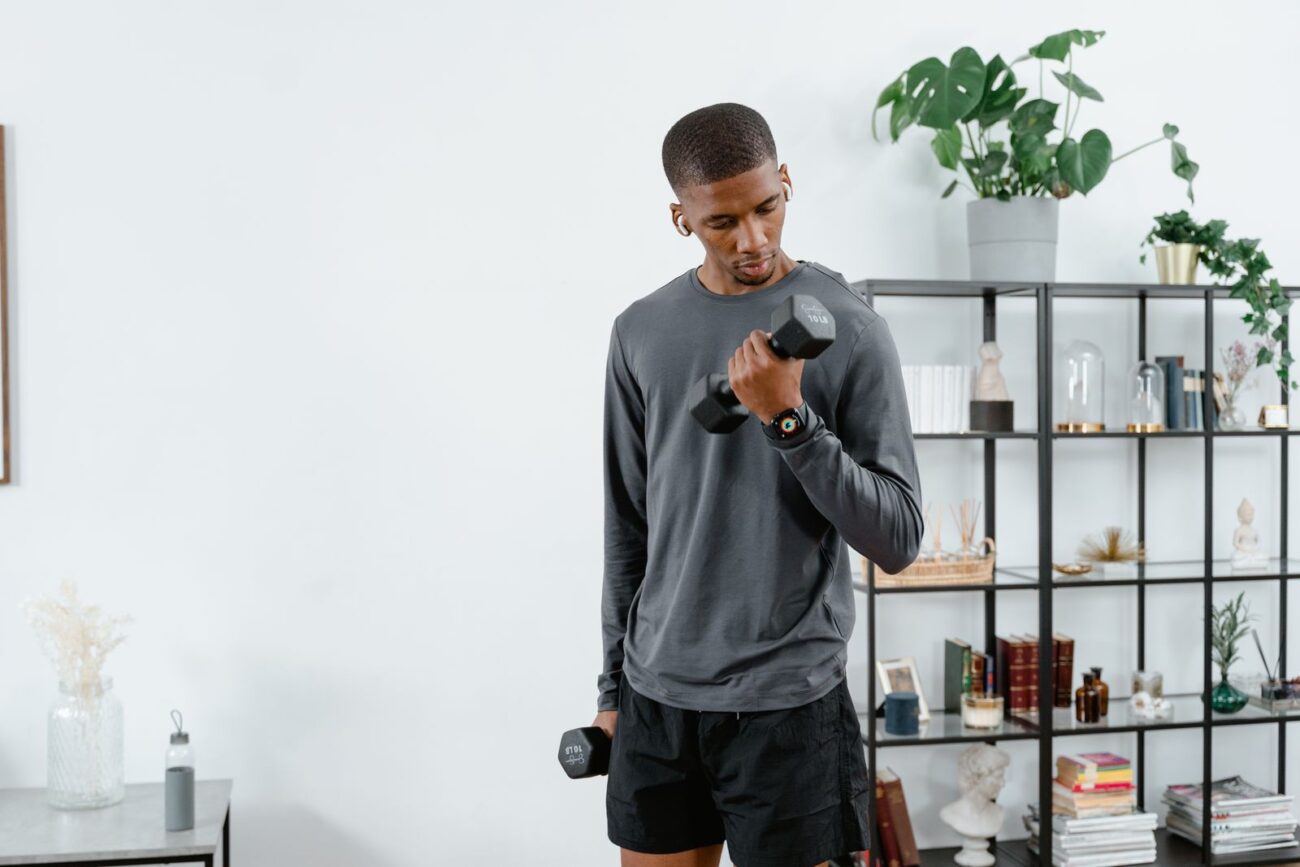 A man doing dumbbell curls at home in a living room, showing how to build muscle at home with simple equipment