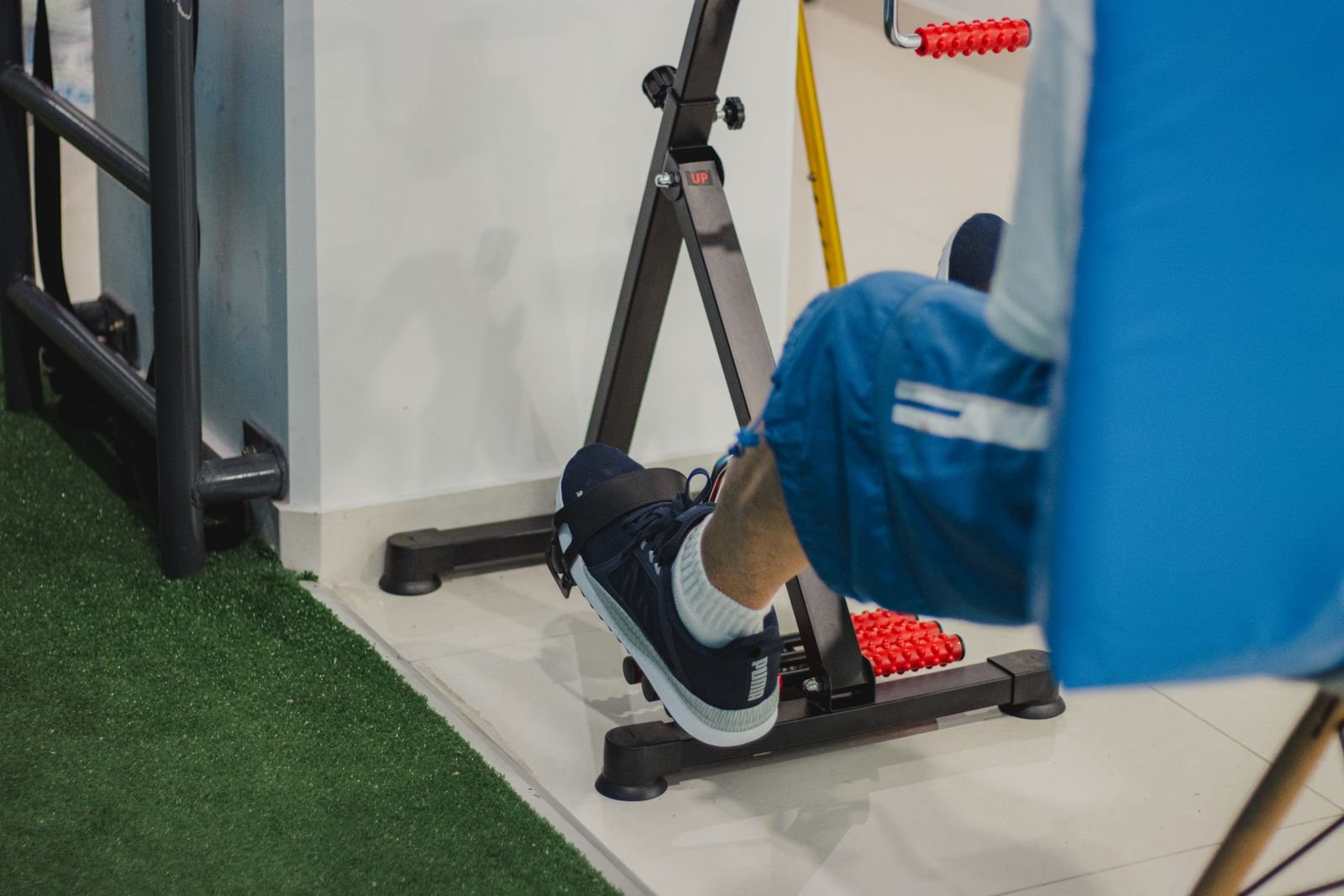Person seated on a chair using a mini pedal stepper machine for low-impact lower body exercise