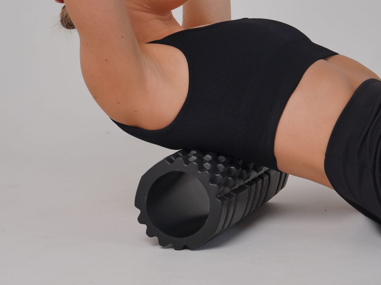 Close-up of a woman lying back on a textured black foam roller for myofascial release