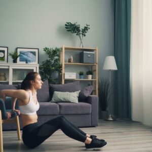 Woman doing tricep dips at home using a chair for support, promoting fitness indoors.