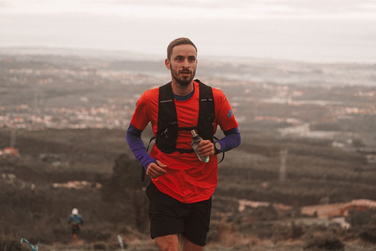 Male athlete running outdoors on a scenic trail wearing a snug-fit black weighted running vest backpack