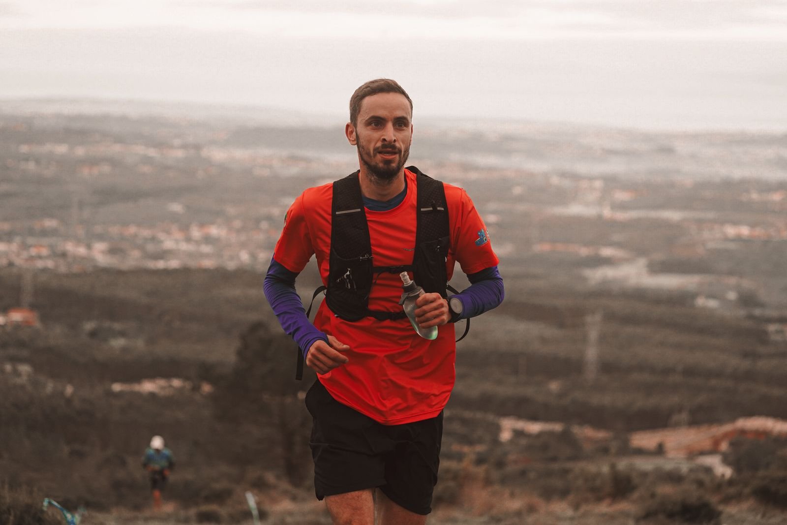 Male athlete running outdoors on a scenic trail wearing a snug-fit black weighted running vest backpack