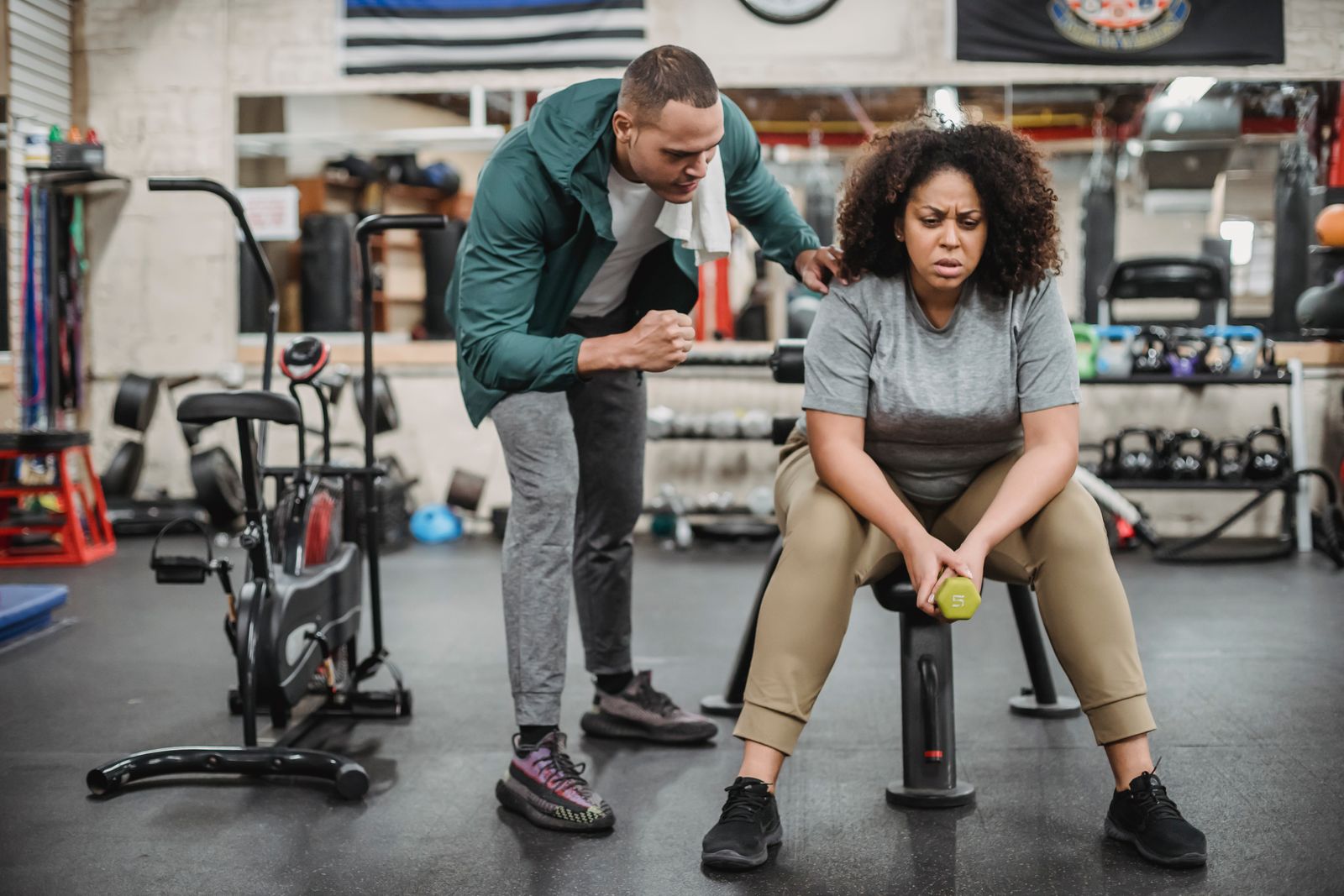 A personal trainer coaching a client through a dumbbell exercise in a gym