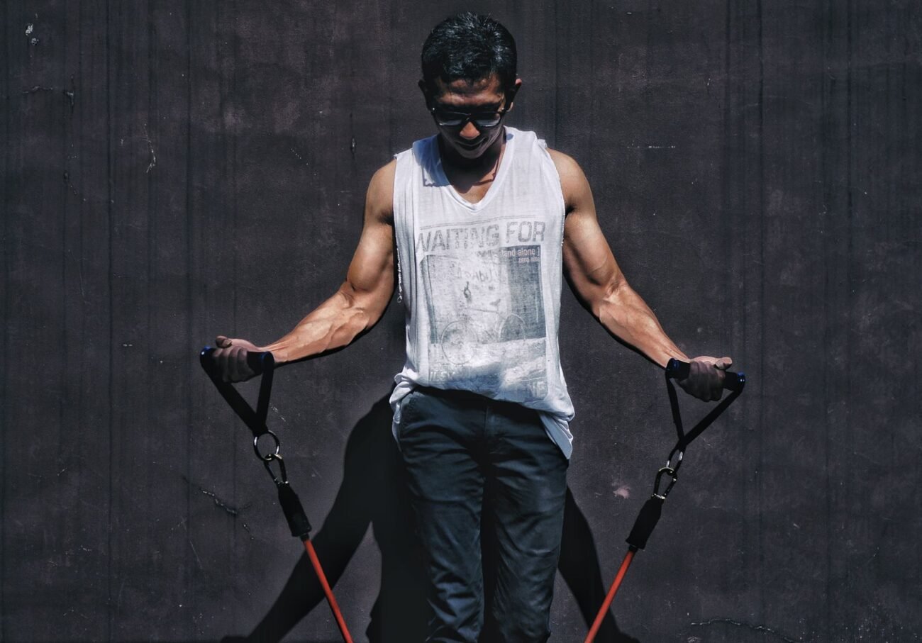 Man performing bicep curls using red resistance bands with foam handles outdoors against a dark wall