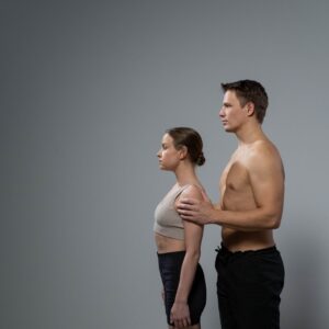 A shirtless man and a woman standing with tall, upright posture