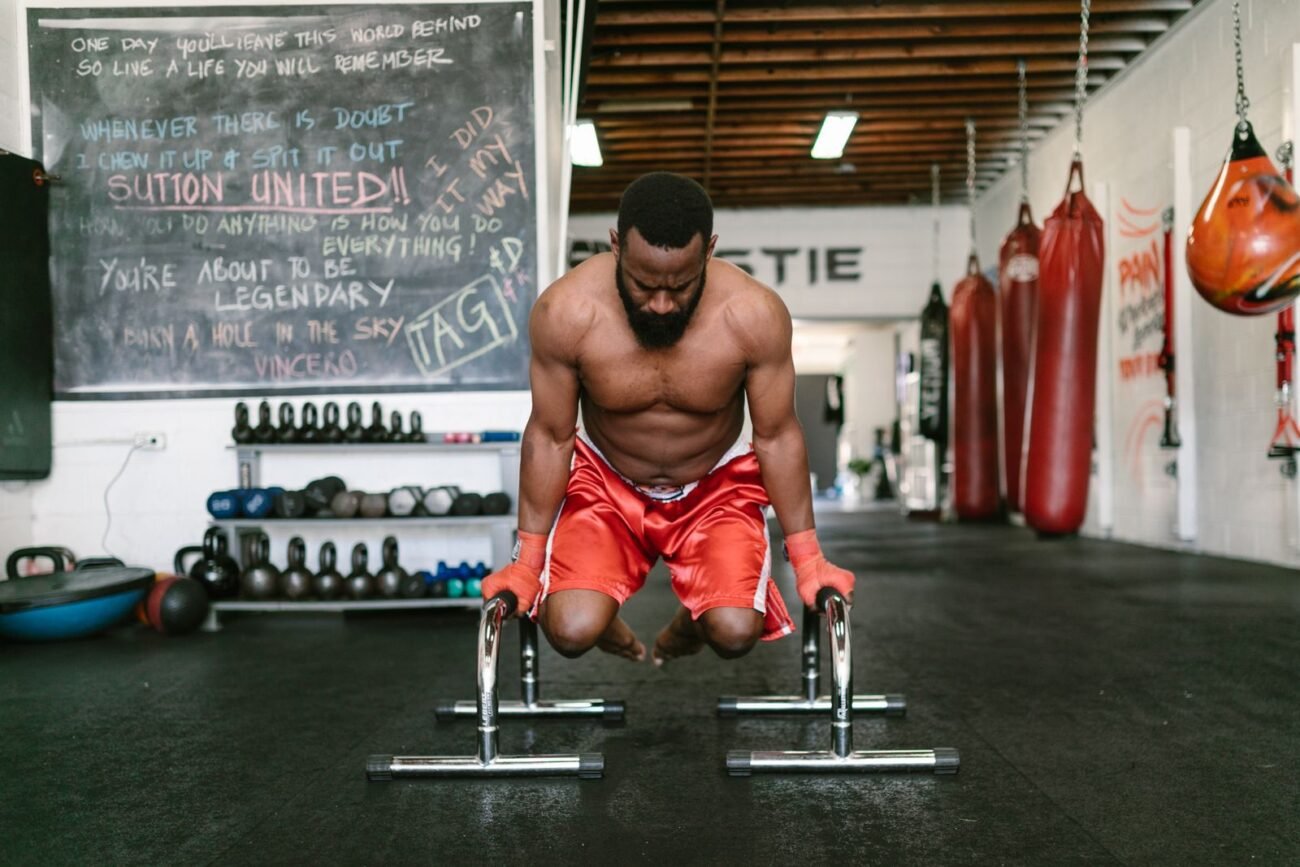 Muscular man performing bodyweight dips on low parallette dip station bars in a gym setting